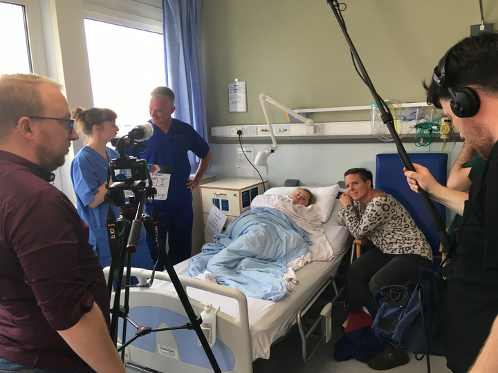 A film crew in a hospital room set with a Hijinx actor lying in a hospital bed 
