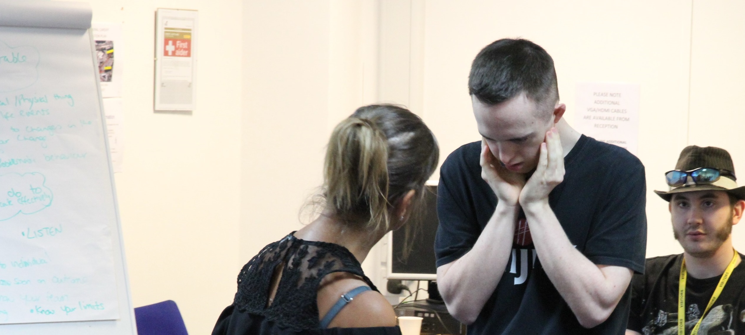 A Hijinx actor, performing a role play scenario, holding their head in their hands with another actor facing them. 