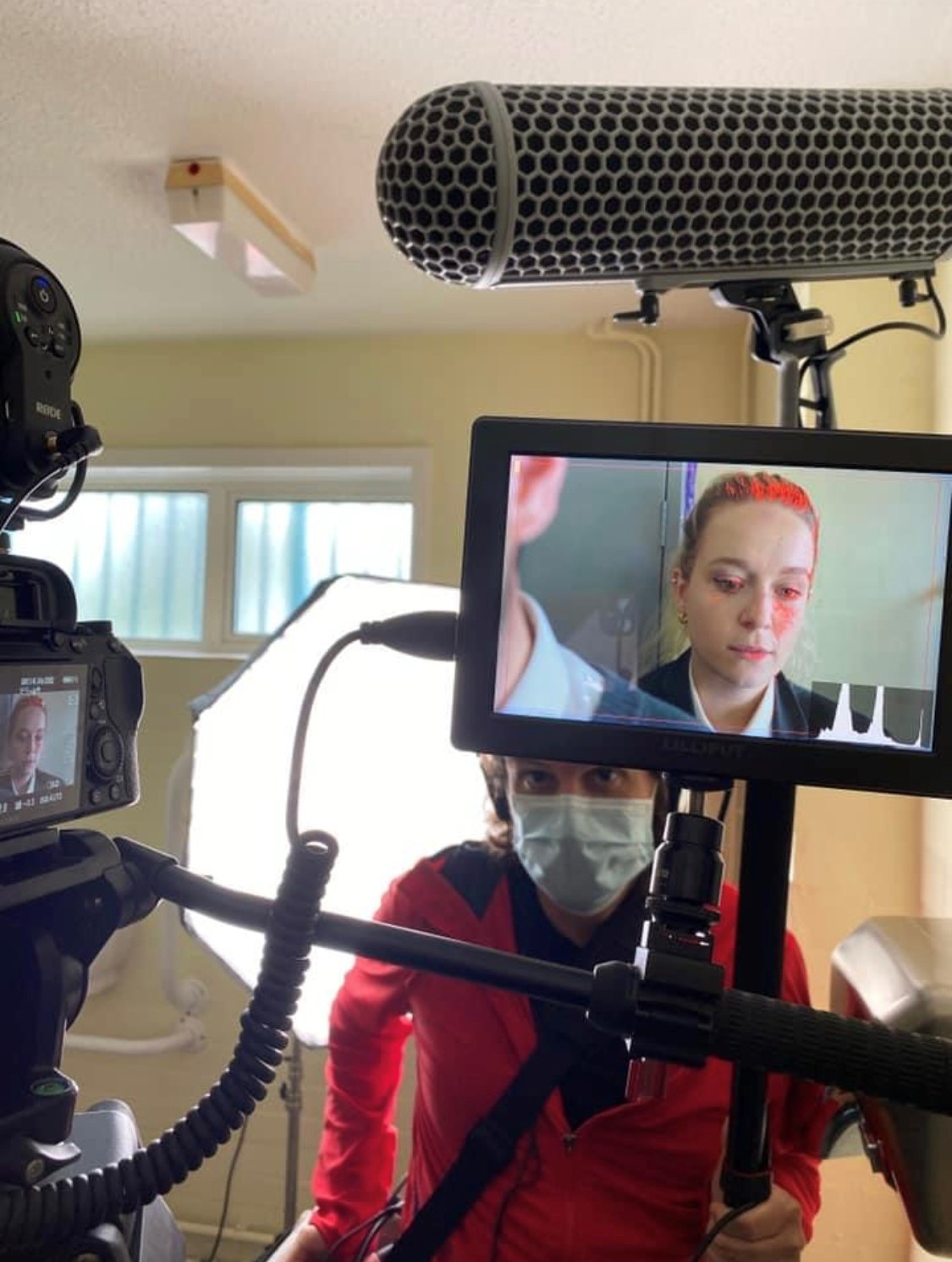 Film equipment on set in a school bathroom. The camera screen shows a young girl in uniform looking down.