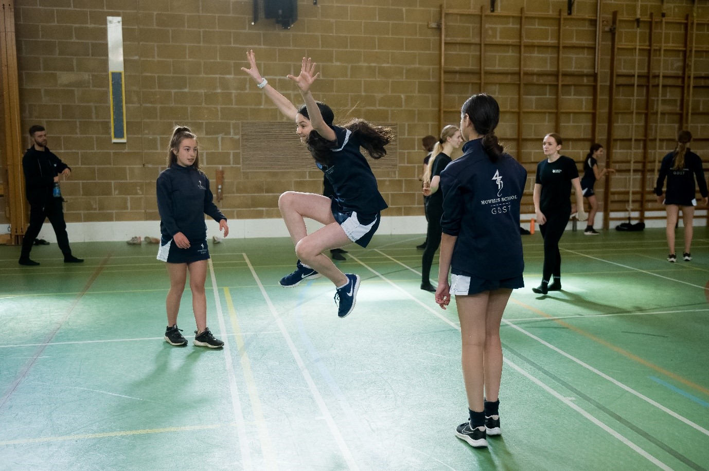 A group of school students and Rubicon dancers in a gym hall. One student is jumping in the air. 