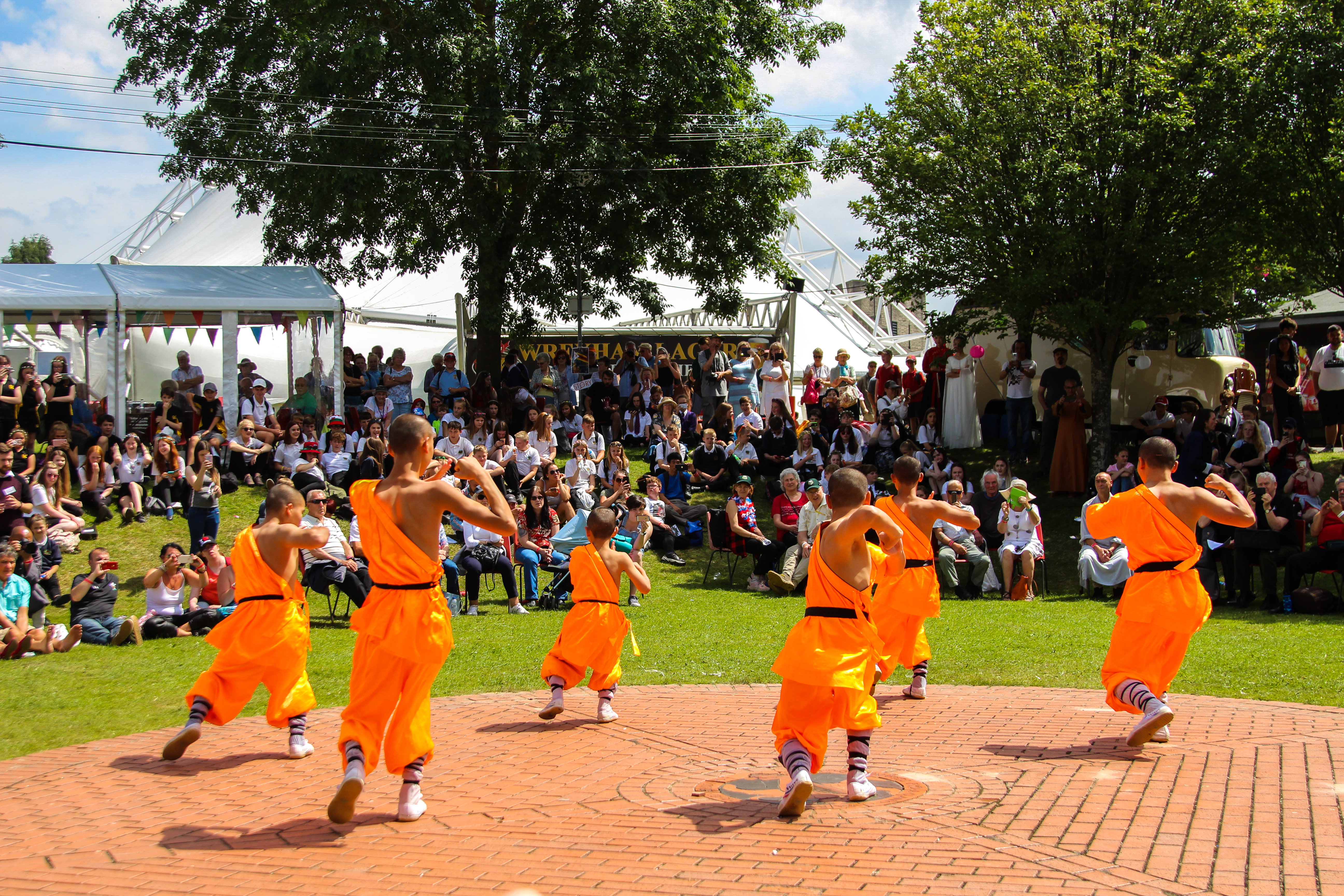 Six young dancers dressed in bright orange robes performing outdoors at Llangollen International Musical Eisteddfod