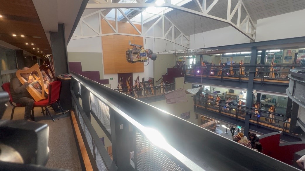 The inside of a building with four visible interior balconies. Each one of the balconies is full of musicians playing harps. 