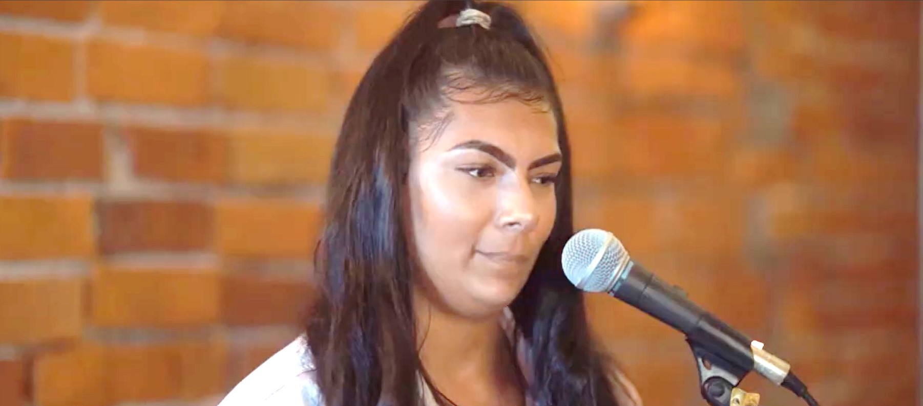 A performer in front of a microphone with a brick wall in the background.