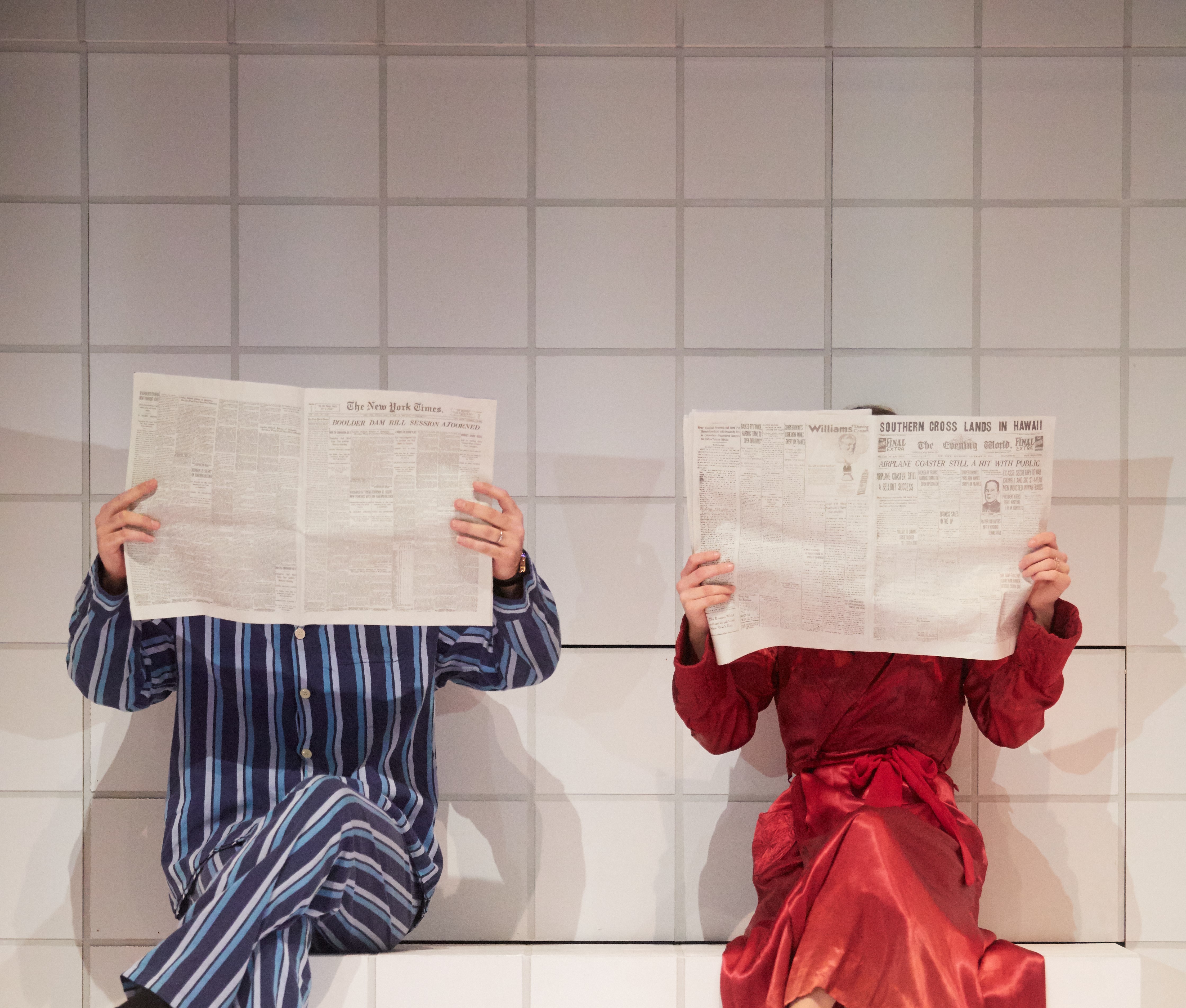 A man and a woman in nightwear in bed reading newspapers as part of Royal Welsh College of Music & Drama’s ‘Machinal’. Photo by Mark Douet  