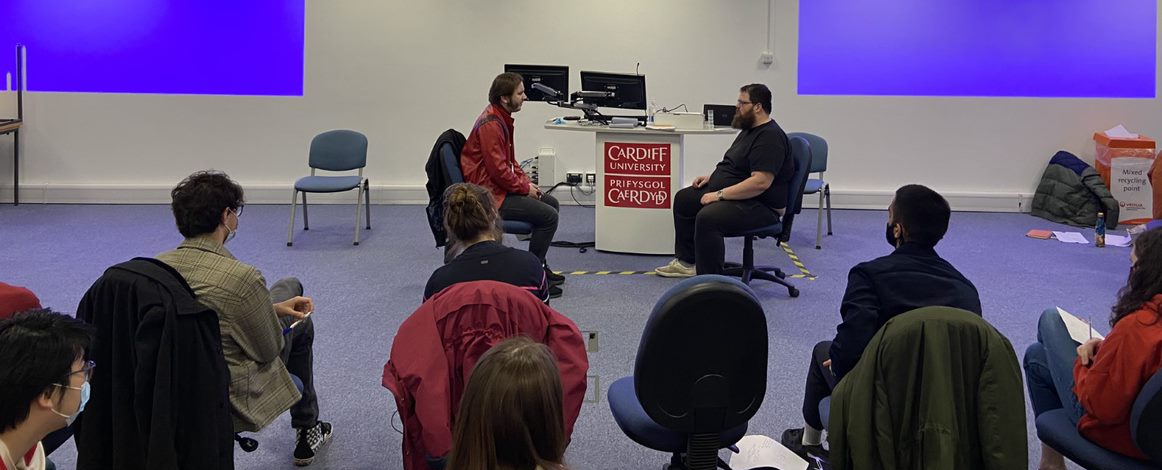 A group of srudents sat facing a Hijinx actor and another student sat at the front of the room. 