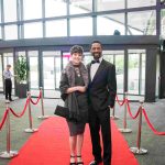 Two people standing on a red carpet and smiling