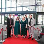 Six people standing on a red carpet and smiling