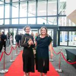 Two people standing on a red carpet and smiling