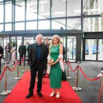 Two people standing on a red carpet and smiling