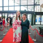 Two people standing on a red carpet and smiling