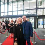 Two people standing on a red carpet and smiling