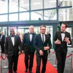 Four people walking down a red carpet and smiling