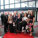 Ten people standing on a red carpet and smiling