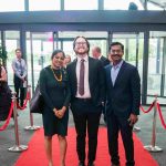 Three people standing on a red carpet and smiling