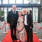 Three people standing on a red carpet and smiling