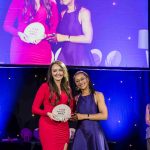 Actor Suzanne Packer and the winner of the Adviser of the Year Award, Gemma Barnett, on a presentation stage holding the award and smiling at the camera