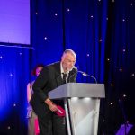 Actor Julian Lewis Jones standing behind a lectern on a presentation stage