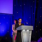 Actor and playwright Azuka Oforka standing behind a lectern on a presentation stage