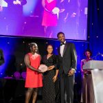 Actor and playwright Azuka Oforka and two people from MLArt standing on stage holding an award and smiling at the camera