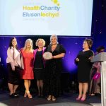 People from Cardiff & Vale Health Charity standing on stage with Grammy Award-winning Soprano Rebecca Evans, holding an award and smiling at the camera