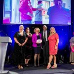 People from Cardiff & Vale Health Charity standing on stage with Olympic athlete and broadcaster Colin Jackson, holding an award and smiling at the camera