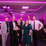 The Robert Maskrey Award for Arts Philanthropy winners Alan and Sonja Jones holding the award, smiling at the camera with people from NEW Sinfonia