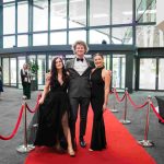 Three people standing on a red carpet and smiling